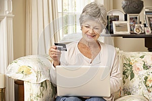 Retired Senior Woman Sitting On Sofa At Home Using Laptop To Make Online Purchase