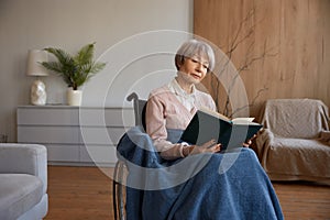 Retired woman with disability sitting in wheelchair reading book