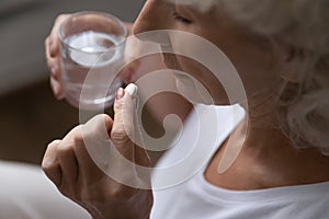 Retired woman holding pill and glass of water.