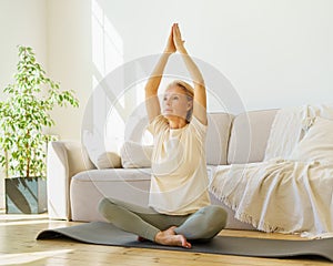 Retired woman in lotus pose practicing yoga exercises at home, sitting on mat and meditating