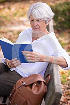 retired woman reading book on bench