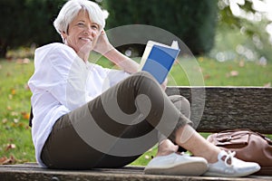 retired woman reading book on bench