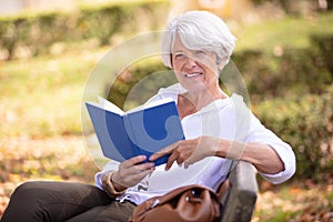 retired woman reading book on park bench