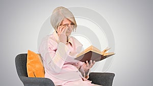 Retired woman reading a book sitting on a chair on gradient back