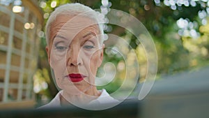 Retired woman reading newspaper in city park portrait. Focused stylish lady