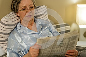 Retired woman reading newspaper before sleeping