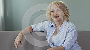 Retired woman sitting on couch, looking at camera and smiling, happy pension