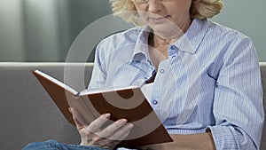 Retired woman sitting on couch and reading book, avid book reader, leisure time