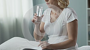 Retired woman taking pill, drinking it up with water, health troubles medication