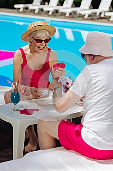 Retired woman wearing red sunglasses playing cards with husband