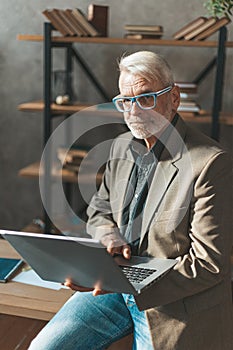 Retired work. A provincial man in a suit sits at the table and holds a laptop in his hands. The old man uses modern technology