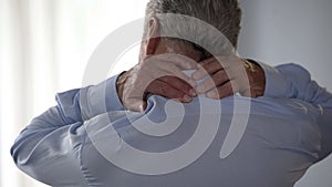 Retiree man rubbing back of his neck, standing backwards, office desk worker