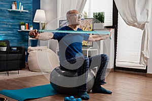 Retiree senior man sitting on swiss ball in living room doing healthcare fitness exercises