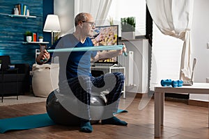 Retiree senior man sitting on swiss ball in living room doing healthcare fitness exercises