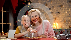 Retiree woman and granddaughter decorating Xmas cookies smiling in camera