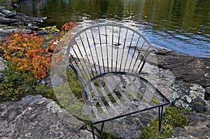 Retirement Living - An outdoor chair sitting on a rocky shore with a calm lake and autumn leaf color