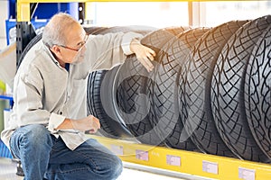 Retirement man touching and choosing for buying a tire in a supermarket mall. Measuring rubber car wheel