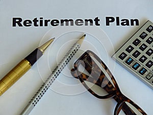 Retirement plan note written on a white paper. A pair of brown frame glasses, pen and pencil, calculator.