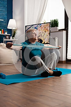 Retirement senior woman sitting on yoga mat stretching legs muscles using stretch elastic band