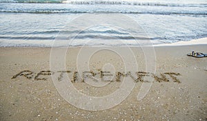 Retirement written on sand by sea at beach.