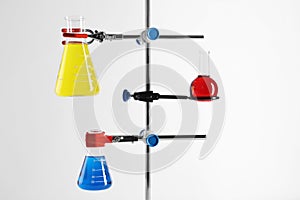 Retort stand and laboratory flasks with liquids on white background