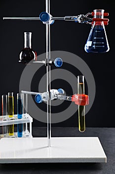 Retort stand and laboratory glassware with liquids on table against black background