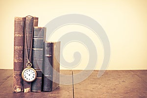Retro aged books, pocket watch on oak wooden table. Vintage style filtered photo