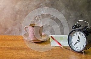 Retro alarm black clock vintage style with Blank open book, red pencil and cup coffee pastel pink old on wooden table.