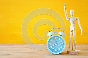 Retro alarm clock next to wooden dummy doll over yellow background