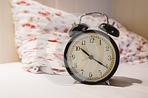 Retro alarm clock with 10 O`clock and twenty minuet, on white bed with pillow photo