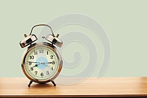 Retro alarm clock on old wooden table on green wall