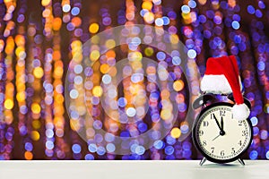 Retro alarm clock with Santa Claus hat against amazing Christmas fairy bokeh lights background. Copy space