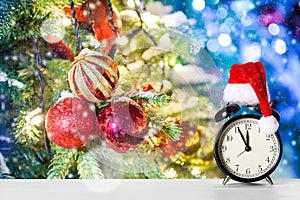 Retro alarm clock with Santa Claus hat against amazing Christmas tree background with Christmas toys, lights and snow