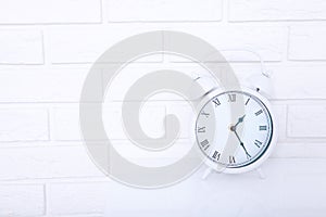 Retro alarm clock with twenty five minutes past one o`clock near brick wall on white workplace. Selective focus