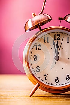 Retro alarm clock with two minutes to midnight. Filtered photo in vibrant colors 50s to 60s. Pink background