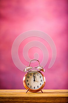 Retro alarm clock with two minutes to midnight. Filtered photo in vibrant colors 50s to 60s. Pink background