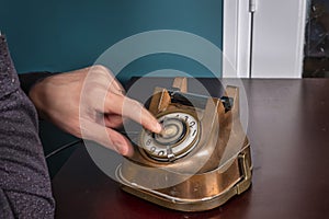 Retro antique classic outdated copper with black color rotary telephone from circa 1950s on wooden table, green wall