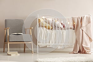 Retro armchair next to white wooden crib with pastel bedding