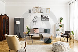 Retro armchair and pouf on the cozy carpet in contemporary living room interior with grey sofa and vintage furniture