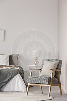 Retro armchair with white pillow next to cozy king size bed with grey bedding in fashionable bedroom interior