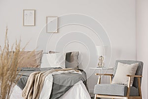 Retro armchair with white pillow next to cozy king size bed with grey bedding in fashionable bedroom interior