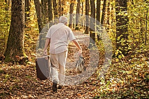 Retro bag is his travel companion. Old man carry travel bag in woodland. Elderly person travel through autumn forest