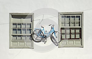 Retro bicycle on exterior wall of cement facade. Two old closed sash windows on white facade and hanging bicycle. Decorative