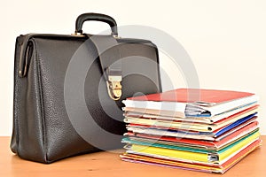 Retro black leather briefcase and stack of files on the brown wooden table