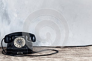 Retro black rotary telephone on wooden table in front gray concrete