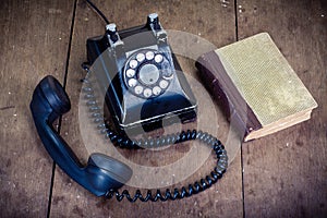 Retro black telephone and book on old oak wooden table. Vintage style photo