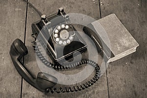 Retro black telephone and book on old oak wooden table. Vintage style sepia photo