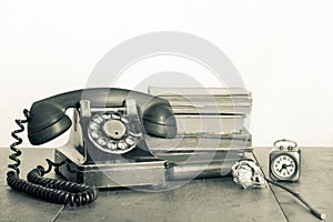 Retro black telephone and books, clock, dried flower on old oak wooden table. Vintage style sepia photo