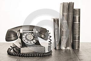 Retro black telephone and books on old oak wooden table. Vintage style sepia photo