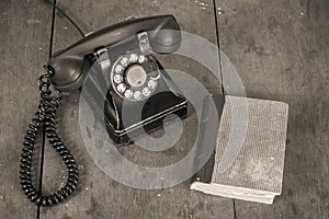 Retro black telephone and books on old oak wooden table. Vintage style sepia photo